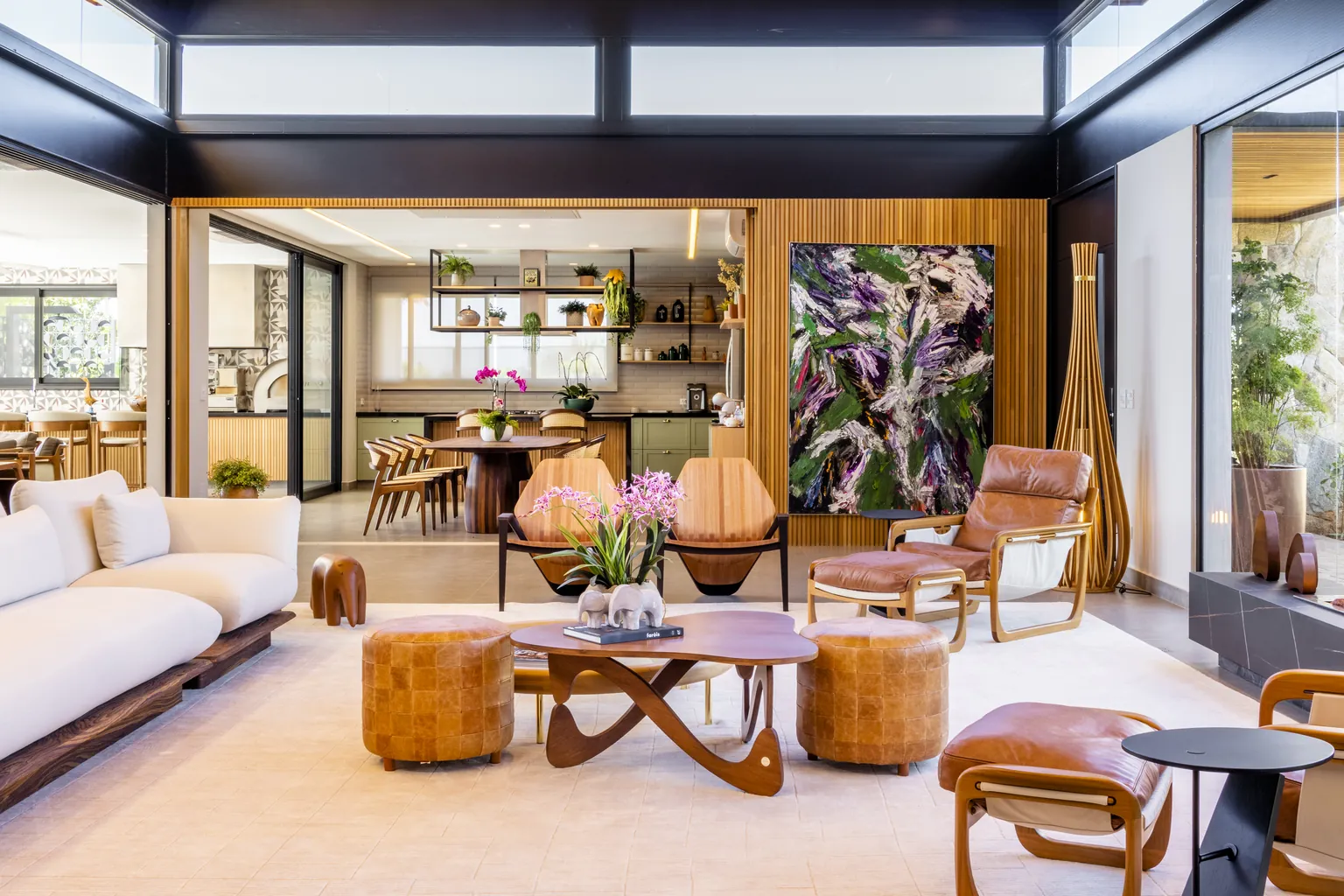 O mesmo ambiente pronto: sala com poltronas de couro e madeira, pufe de couro, mesa de centro orgânica e tela colorida