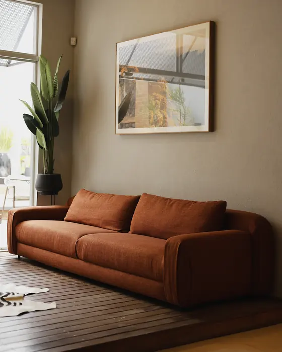 Showroom DRØM: sofá em tom terracota sobre estrado de madeira, com quadro e planta